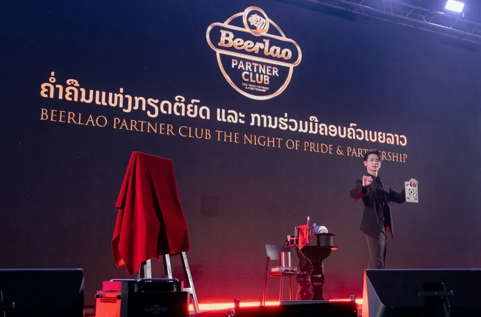 นักมายากลบนเวทีพิธีเปิดงานบริษัท ข้างวัตถุที่คลุมด้วยผ้าสีแดง