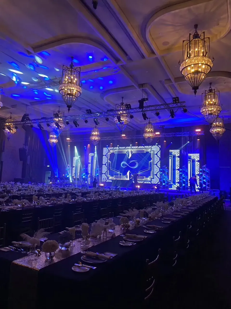 ห้องบอลรูมจัดโต๊ะกาลาดินเนอร์พร้อมเวทีและไฟสีน้ำเงินก่อนเริ่มงาน