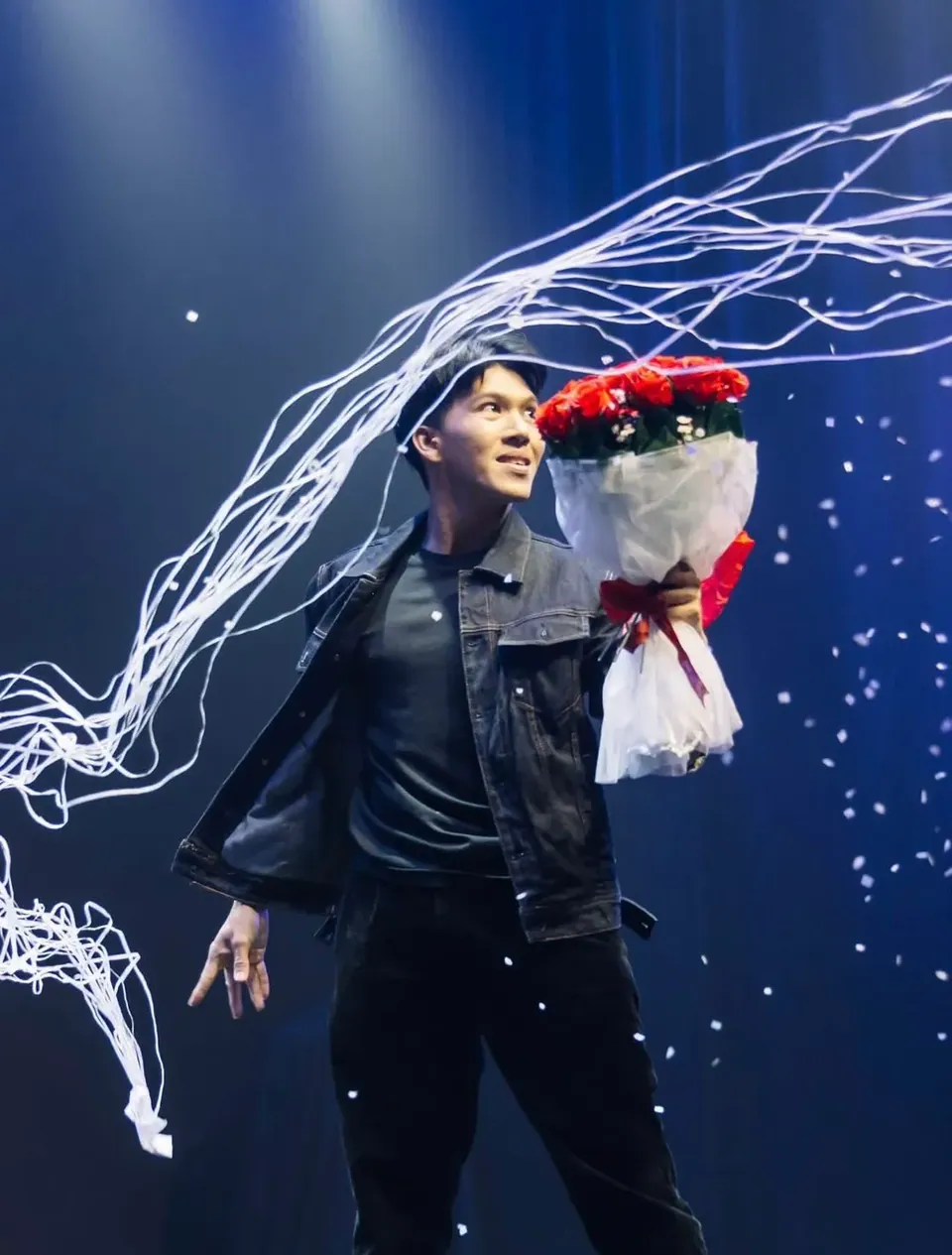 นักมายากลเสกช่อดอกกุหลาบบนเวทีท่ามกลางริบบิ้นสีขาว