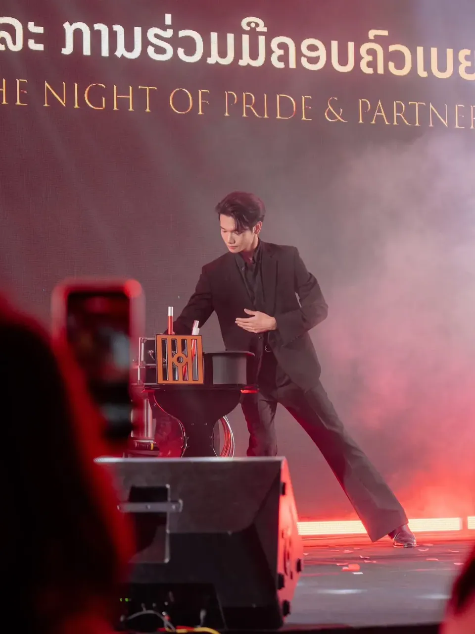นักมายากลแสดงบนเวทีงานเลี้ยงบริษัทท่ามกลางไฟสีแดง