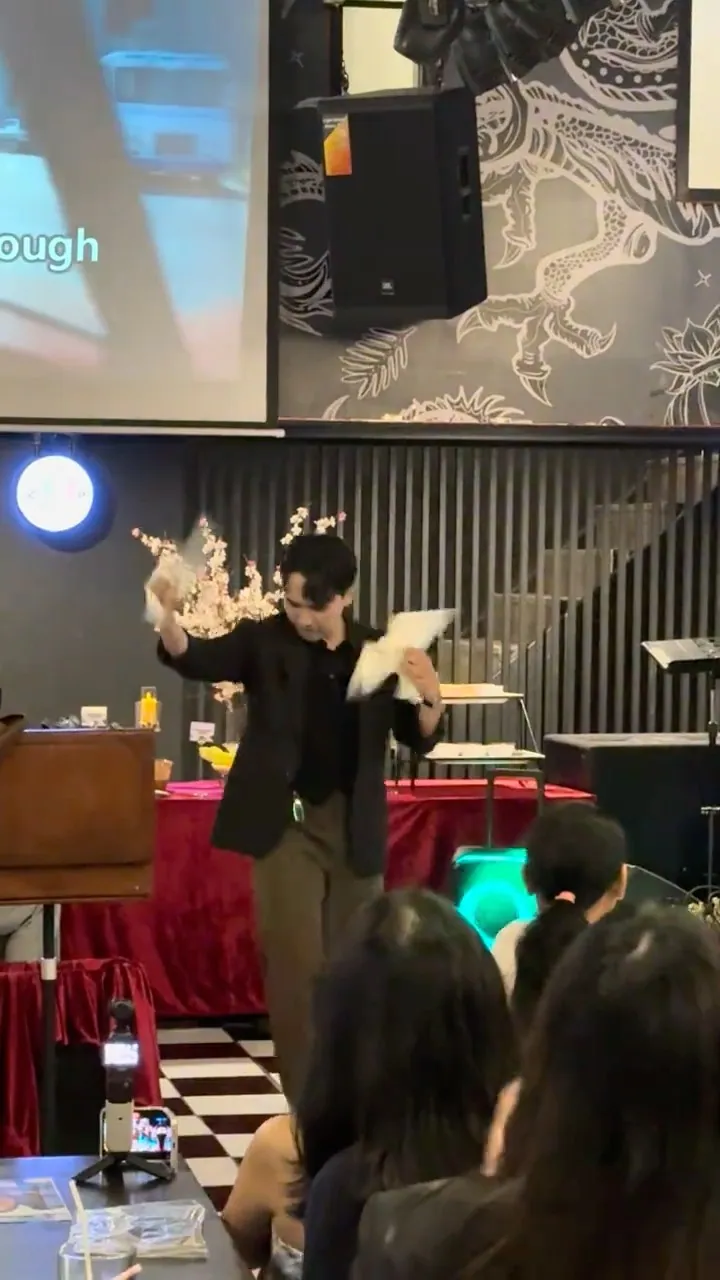 นักมายากลเสกนกพิราบบนเวทีเล็กในร้านอาหาร โดยมีแขกนั่งชมอยู่ใกล้ ๆ